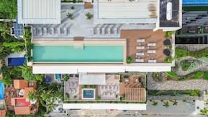 Vista aérea de um hotel com piscina no terraço, área de estar e uma piscina separada com espreguiçadeiras.