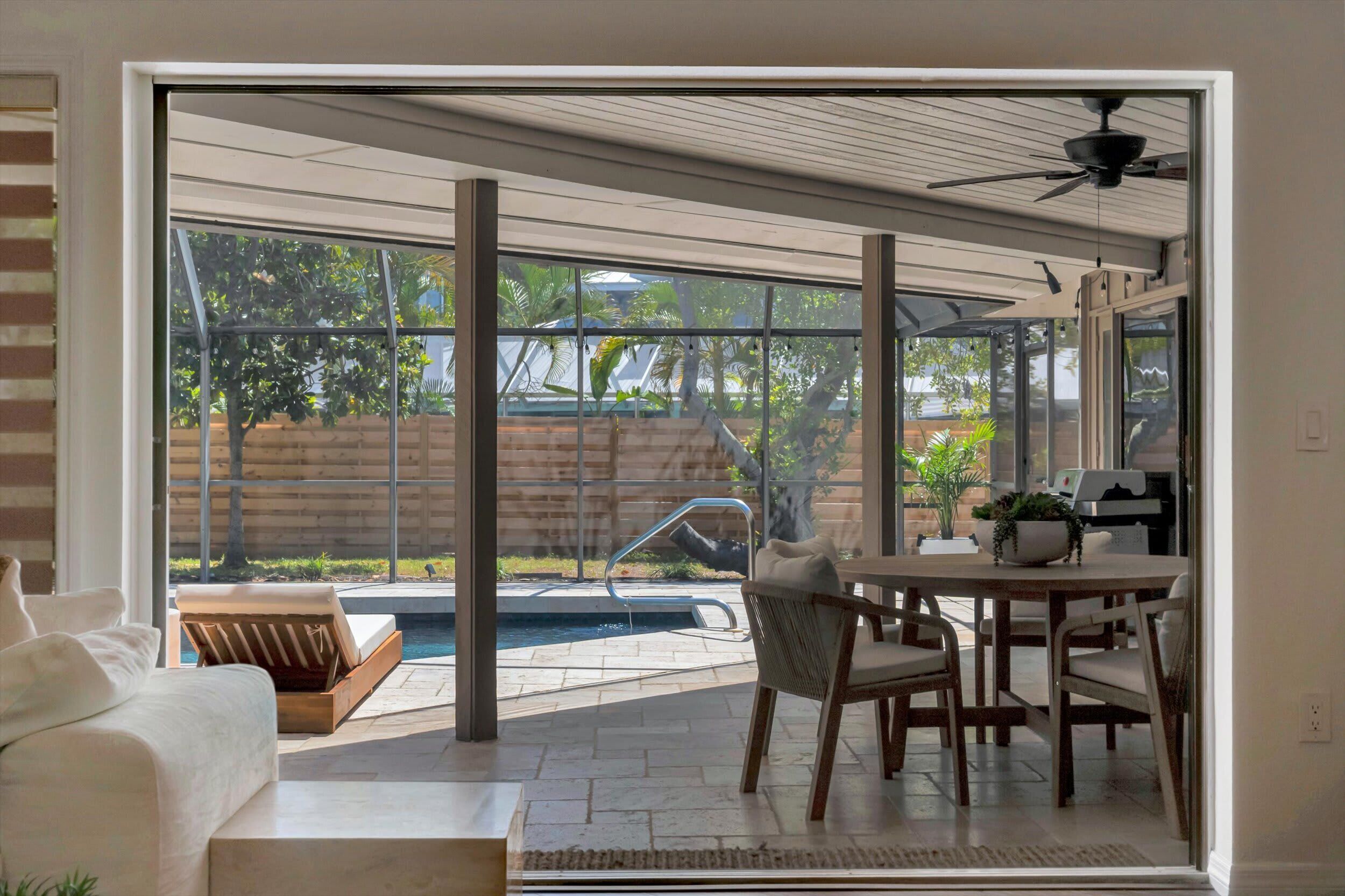 A modern living room with a glass door leading to a patio area with a pool, outdoor furniture, and a ceiling fan.