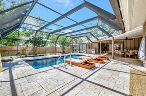 Una piscina scoperta coperta con sedie a sdraio, una zona patio e un'area pranzo.