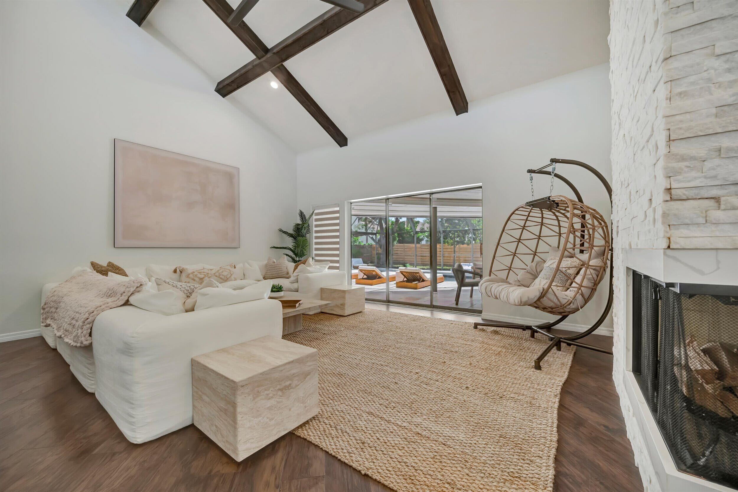 A living room with a white sofa, a hanging chair, a fireplace, and a large window.