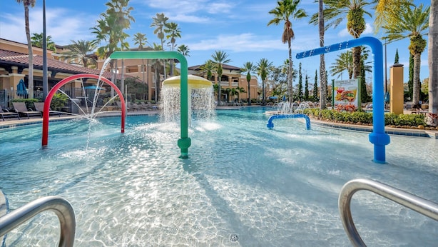 Ein Pool mit Wasserspielen, umgeben von Palmen und Hotelgebäuden.