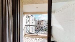 Un balcone con ringhiera in metallo, vista su edifici alti e una porta con tende.