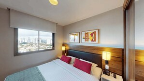 A hotel room with a bed, two bedside lamps, a city view, and two abstract wall art pieces. - Berrini Mood Beautiful 1 BR in S o Paulo (São Paulo)
