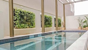 A swimming pool with tiled edges, surrounded by walls with vertical gardens. - Berrini Mood Beautiful 1 BR in S o Paulo (São Paulo)
