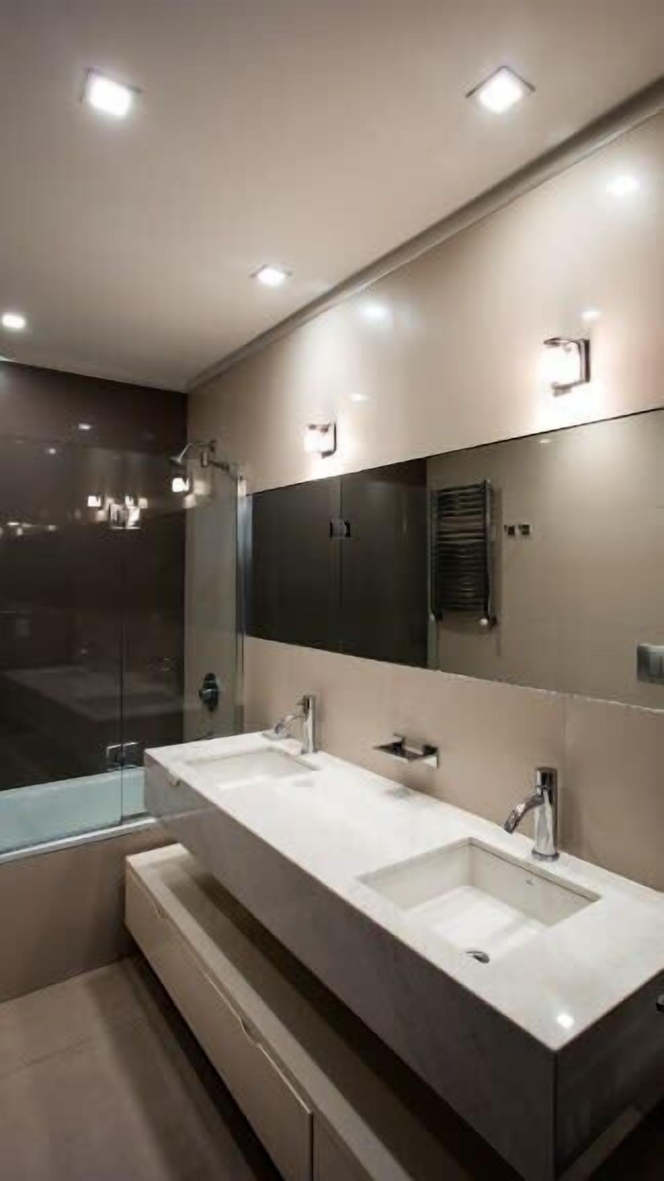 Ein modernes Badezimmer mit zwei Waschbecken, einem großen Spiegel, Einbauleuchten und einem Fenster.