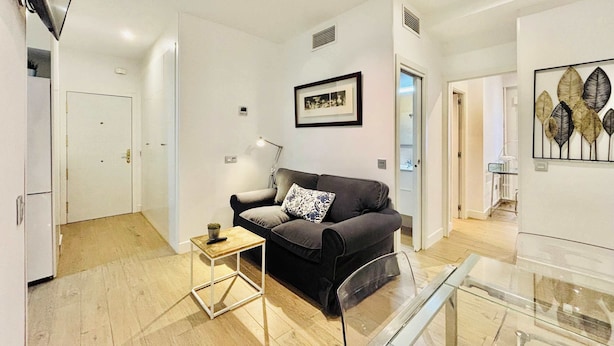 A modern living room with a sofa, a side table, a glass coffee table, and a framed picture on the wall. - Republica 2BR apt Near Madrid s Financial Center (Madrid)