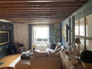 Ein Wohnzimmer mit einer Couch, einem Couchtisch und einem Fernseher. Es gibt einen Balkon mit Geländer und einer Pflanze.