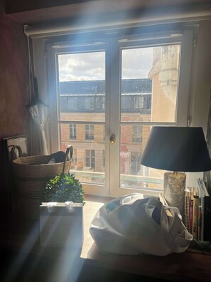 Ein Zimmer mit großem Fenster, einer Lampe, einem Korb, einer Pflanze und einer Tasche auf einem Tisch.