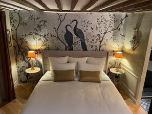 A bedroom with a bed, two bedside lamps, and a wall mural of birds on trees. - Elegance Marais A Distinctive High end Marais one Bedroom (Paris)
