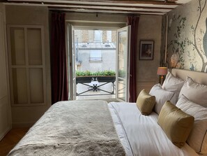 Ein Schlafzimmer mit einem Bett, Blick durch eine offene Tür auf einen Balkon und einer Lampe auf dem Nachttisch.