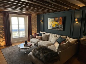 A living room with a sofa, a coffee table, a painting, and a window with curtains. - Elegance Marais A Distinctive High end Marais one Bedroom (Paris)