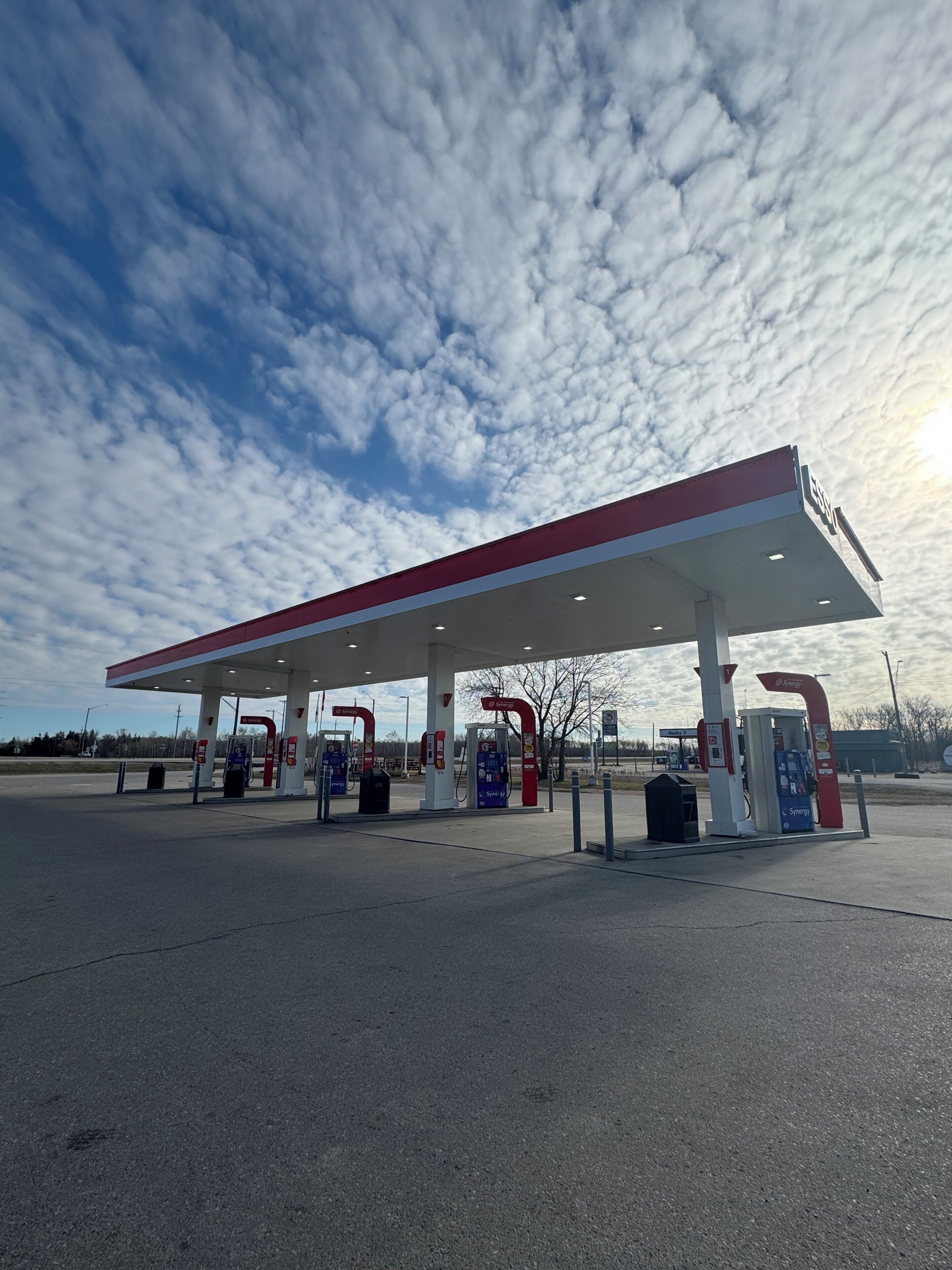 A gas station with multiple fuel pumps, a canopy, and a SYNERGY sign.