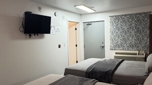 A hotel room with two beds, a flat-screen TV mounted on the wall, a door, and a patterned curtain.
