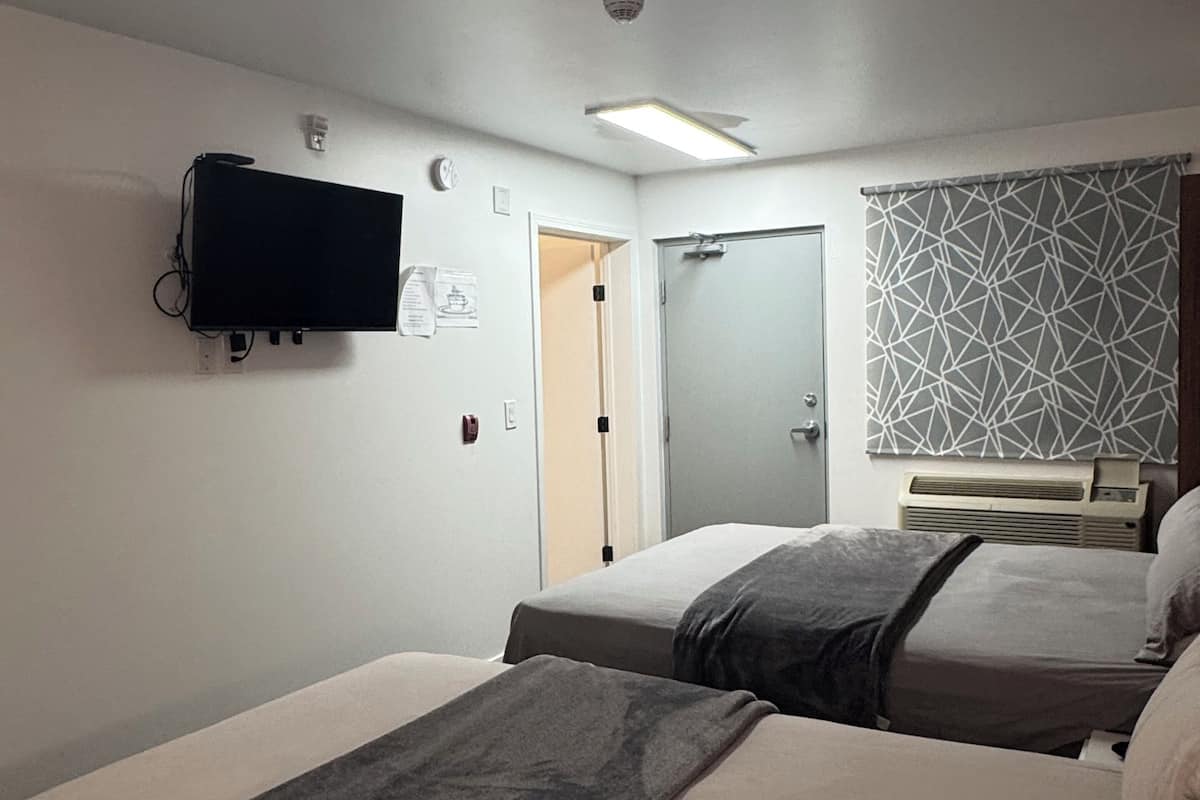 Hotellihuone, jossa on kaksi sänkyä, seinälle asennettu taulutelevisio, ovi ja kuviollinen verho.