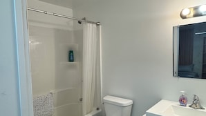 A bathroom with a shower, toilet, sink, and mirror.