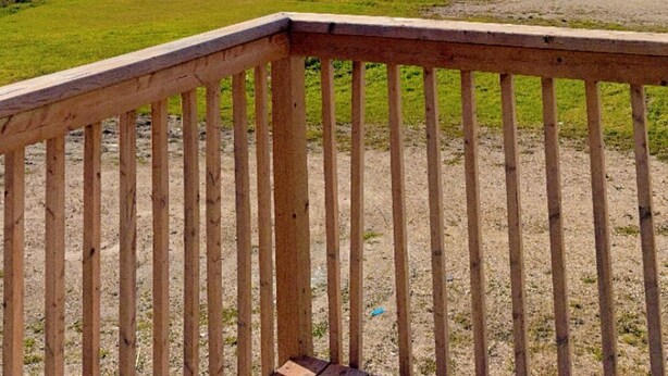 A wooden deck with a view of a grassy field, a trailer, and a distant forest. - Richer Esso and Motel (Richer)