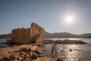 A stone structure with a staircase, located near a body of water with a clear sky and distant hills. - Seaside Plitra Paradiso - Steps From the Beach (Monemvasia)