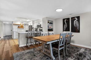 Eine moderne Küche mit weißen Schränken, einem Holztisch und zwei an der Wand hängenden Vogelgemälden.