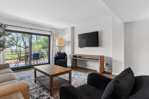 Ein modernes Wohnzimmer mit einer Couch, einem Couchtisch, einem Fernseher und einem Balkon mit Sitzgelegenheiten.