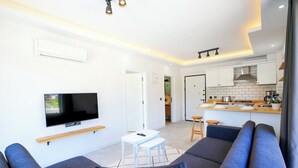 Een moderne woonkamer met een televisie, bank en een kleine eethoek.