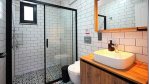 Een moderne badkamer met een douchecabine van glas, een witte wastafel met een houten aanrechtblad, en een spiegel boven de wastafel.
