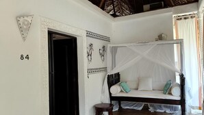 Quarto com cama sob um dossel, porta com número e parede com detalhes decorativos.
