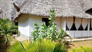 Um edifício com telhado de palha e fachada branca, rodeado por vegetação exuberante.
