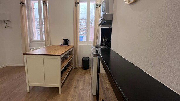 Uma cozinha compacta com bancada de madeira, fogão preto e janela com cortinas.