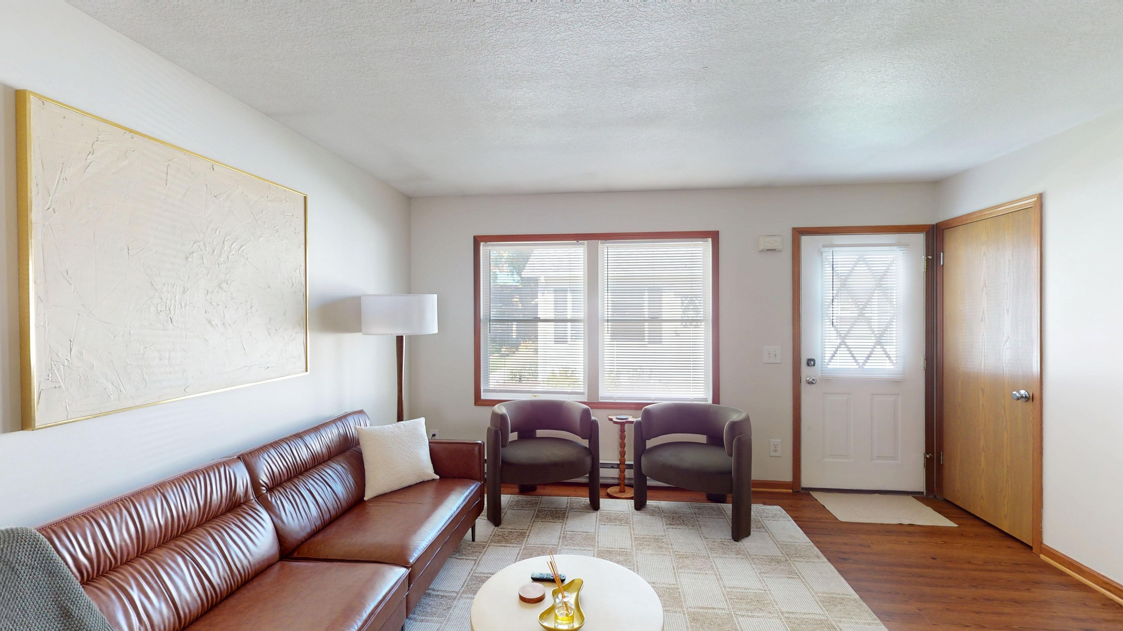 Una sala de estar con un sofá de cuero marrón, dos sillones, una mesa de centro y un cuadro en la pared.