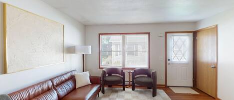 Una sala de estar con un sofá de cuero marrón, dos sillones, una mesa de centro y un cuadro en la pared.