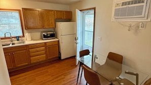 A compact kitchen with wooden cabinets, a refrigerator, a microwave, and a glass dining table with chairs. - Find comfort in this cozy, recently updated apartment. Featuring two bedrooms, a full kitchen with oak cabinets, and a generous living space. It's designed for easy living with a ranch-style, step-up entry. Located in a peaceful neighborhood. (Marion)