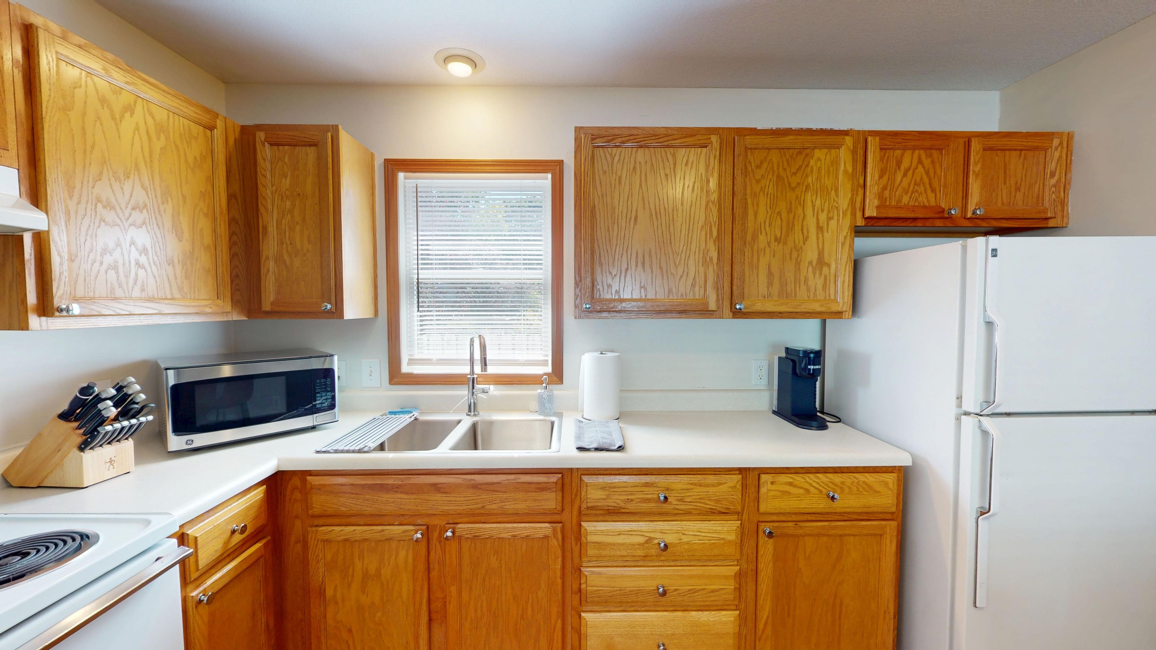 A kitchen with wooden cabinets, a microwave, a sink, and a refrigerator.
