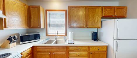 A kitchen with wooden cabinets, a microwave, a sink, and a refrigerator.