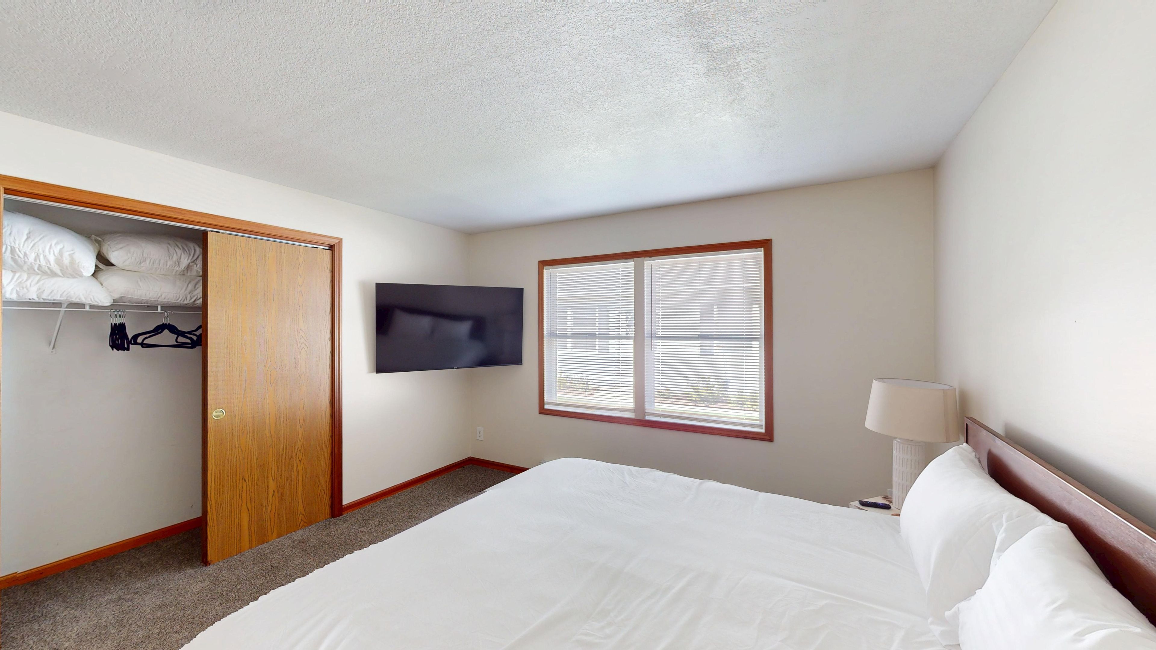 A bedroom with a bed, a closet, a television, and a window with blinds.
