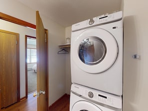A laundry room with stacked washers and dryers, wooden flooring, a door leading to another room, and a small shelf with a hanging item. - Find comfort in this cozy, recently updated apartment. Featuring two bedrooms, a full kitchen with oak cabinets, and a generous living space. It's designed for easy living with a ranch-style, step-up entry. Located in a peaceful neighborhood. (Marion)