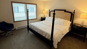 A four-poster bed with white linens, two bedside tables with lamps, a chair, and a window with blinds. - Find comfort in this cozy, recently updated apartment. Featuring two bedrooms, a full kitchen with oak cabinets, and a generous living space. It's designed for easy living with a ranch-style, step-up entry. Located in a peaceful neighborhood. (Marion)
