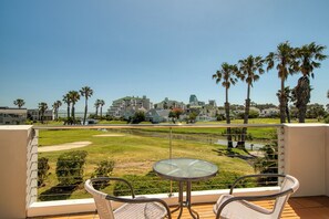 Un balcon avec deux fauteuils en osier et une table en verre, donnant sur une pelouse bien entretenue et un terrain de golf.