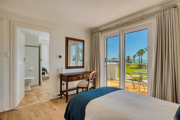 A hotel room with a bed, a desk, a chair, a mirror, a bathroom, and a balcony with a view.