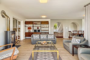A living room with a sofa, coffee table, and a TV. There is a kitchen area with cabinets and a dining table.