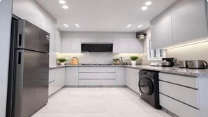 A modern kitchen with stainless steel appliances, a flat-screen TV, and a built-in washing machine. - Chic Stays - 3BR in Mountain View ICity October (Giza Governorate)