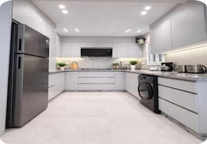 A modern kitchen with stainless steel appliances, a flat-screen TV, and a built-in washing machine. - Chic Stays - 3BR in Mountain View ICity October (Giza Governorate)
