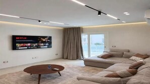 A modern living room with a flat-screen TV, a sofa, a coffee table, and a large window. - Chic Stays - 3BR in Mountain View ICity October (Giza Governorate)