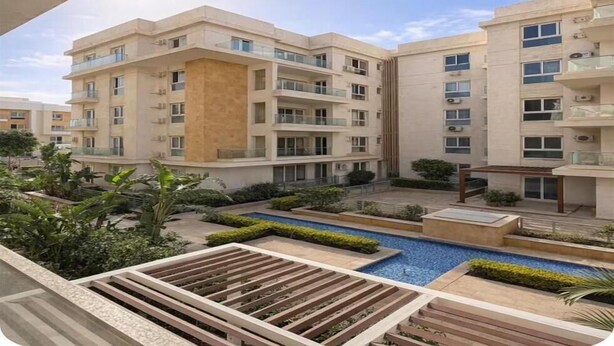 A modern residential building with multiple balconies, a central courtyard with a swimming pool, and surrounding greenery. - Chic Stays - 3BR in Mountain View ICity October (Giza Governorate)