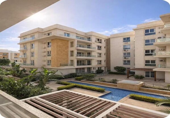 A modern residential building with multiple balconies, a central courtyard with a swimming pool, and surrounding greenery. - Chic Stays - 3BR in Mountain View ICity October (Giza Governorate)