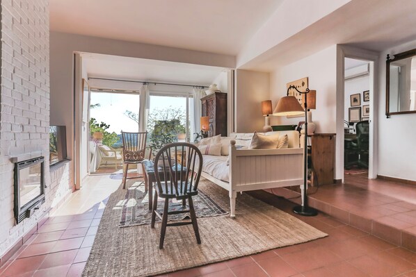Una sala de estar con chimenea, un sofá, una silla, una lámpara y vistas al exterior.