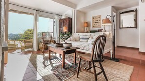 Ein geräumiges Wohnzimmer mit einer großen Glasschiebetür, die auf einen Balkon führt, einem Holztisch mit Stühlen, einem Sofa und einer Lampe.