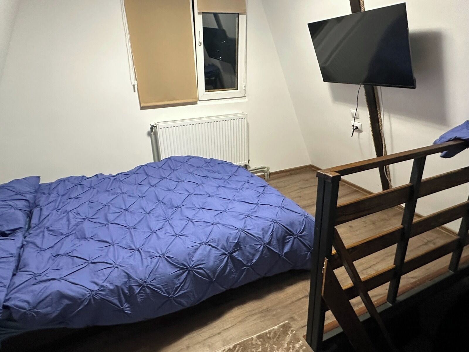 Et soveværelse med seng, et vindue, en radiator og et fjernsyn ophængt på væggen.