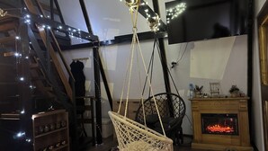A cozy living room with a hanging chair, a fireplace, a TV mounted on the wall, and a staircase.