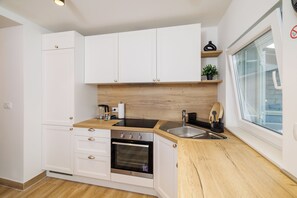 Eine kleine Küche mit weißen Schränken, einer Holz Arbeitsplatte, einem eingebauten Backofen, einem Spülbecken und einem Fenster mit Blick.
