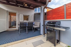 Eine Terrasse im Freien mit Grill, Tisch mit Stühlen und einer überdachten Sitzgelegenheit.